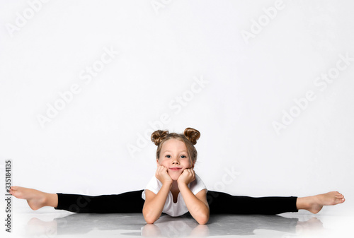 Smiling kid girl does gymnastic exercises at home splits bend forward with her head leaning her hands