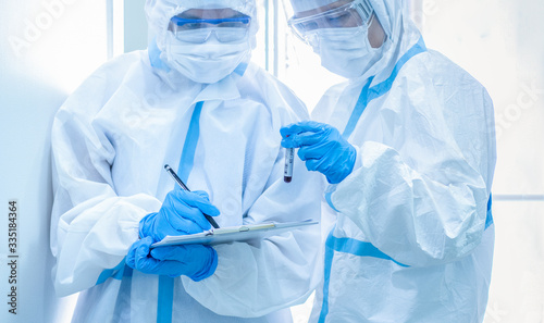 Asian woman doctor in personal protective suit with mask writing on quarantine patient chart, holding test tube with blood sample for screening coronavirus. Coronavirus, covid-19 concept.