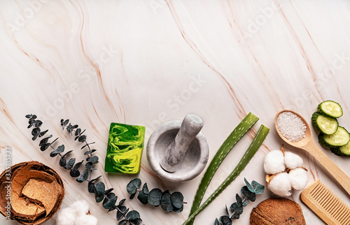 Natural organic cosmetics with aloe vera, sea salt, coconuts, eucaliptys, cotton and cucumber slices top view on white marble background photo