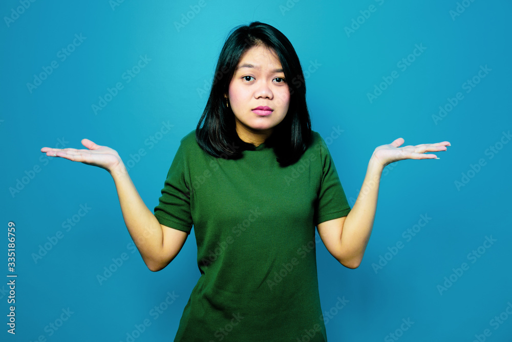 Portrait of Young beautiful asian women using Green T-shirt with blue isolated background, look at the camera and make confused gesture Portrait of Young beautiful asian women using Green T-shirt with blue isolated background, look at the camera and make confused gesture