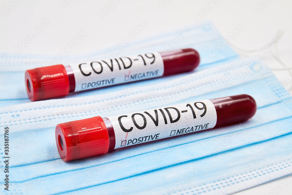 Obraz premium Conceptual photo. Blood test samples for presence of coronavirus on the face protective madical masks. Tubes containing blood samples that have tested positive and negative for coronavirus. Closeup