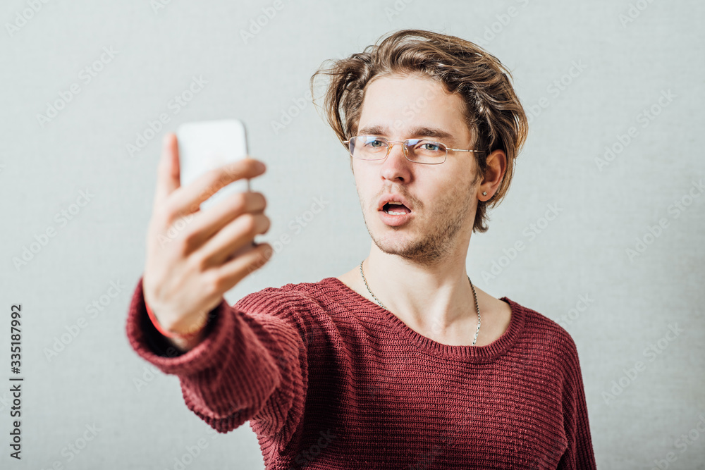 Cheerful selfie. Cheerful young man making photo of himself while standing against grey background Cheerful selfie. Cheerful young man making photo of himself while standing against grey background