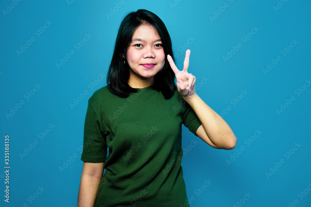 Portrait of Young beautiful asian women using Green T-shirt with blue isolated background, showing peace sign and smiling, Victory sign, two sign Portrait of Young beautiful asian women using Green T-shirt with blue isolated background, showing peace sign and smiling, Victory sign, two sign