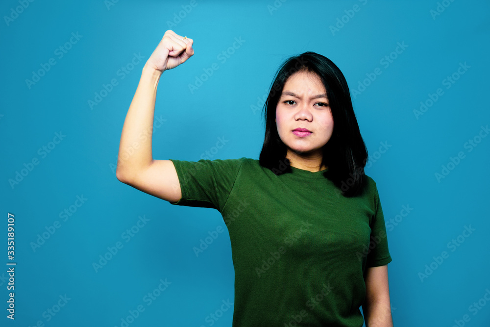 Portrait of Young beautiful asian women using Green T-shirt with blue isolated background, raises arms and shows biceps Portrait of Young beautiful asian women using Green T-shirt with blue isolated background, raises arms and shows biceps
