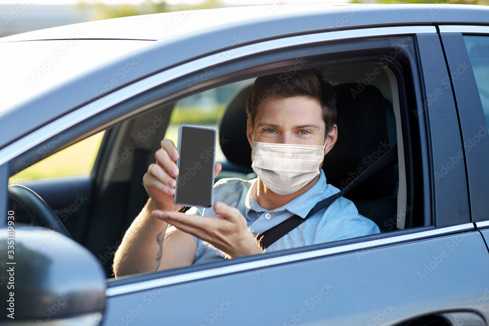health protection, safety and pandemic concept - man or car driver wearing face protective medical mask showing smartphone