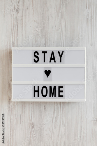 Fototapeta Naklejka Na Ścianę i Meble -  'Stay home' words on a lightbox on a white wooden background, top view. Overhead, from above, flat lay.