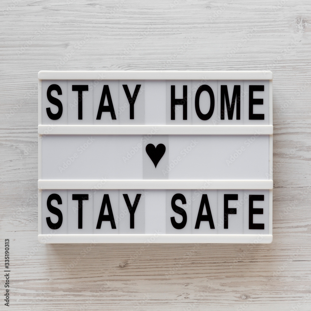 Fotografie 'Stay home stay safe' words on a lightbox on a white wooden surface, top view