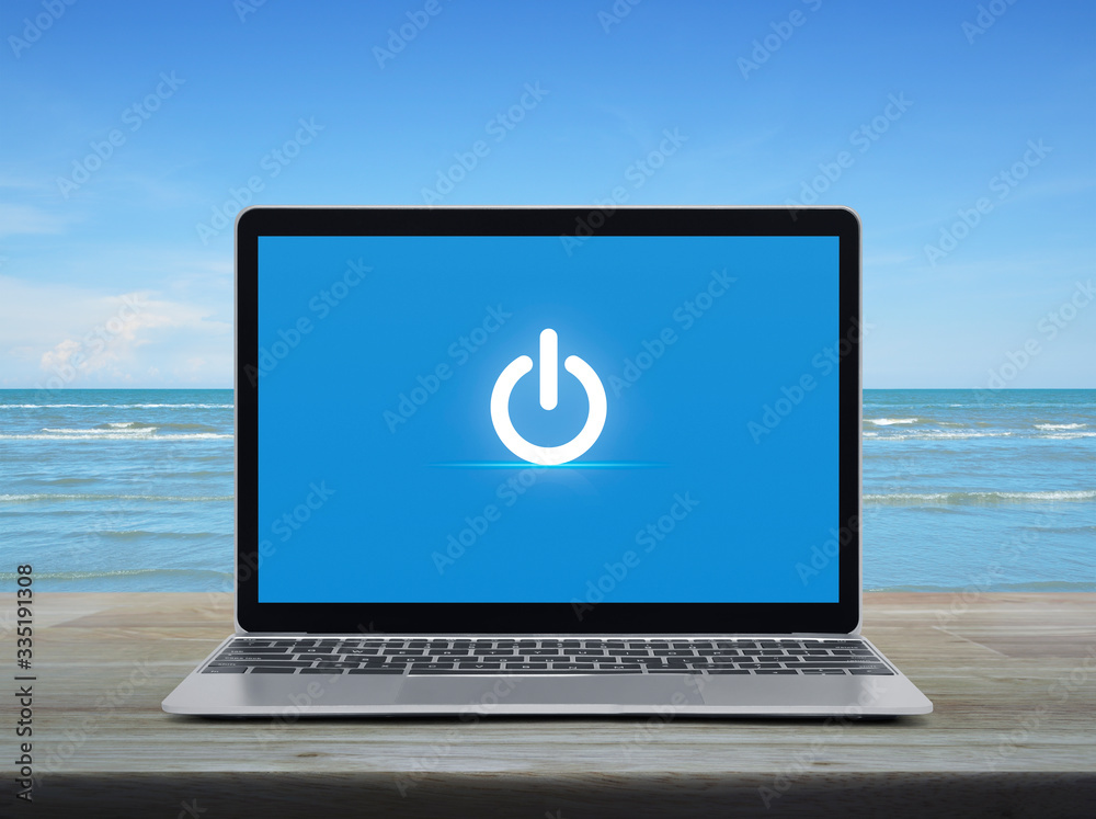 Power button icon on modern laptop computer on wooden table over tropical sea and blue sky with white clouds, Start up business online concept Power button icon on modern laptop computer on wooden table over tropical sea and blue sky with white clouds, Start up business online concept