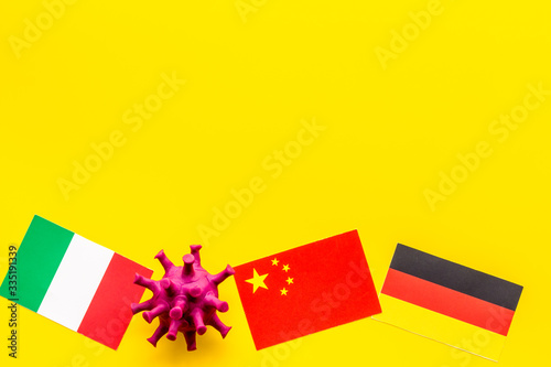 Concept of Corona virus Covid-19 with german, italian and chinease flags on yellow background top-down photo