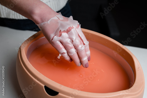 Female hand and orange paraffin wax in bowl. Manicure and skincare. Woman girl in beauty spa salon. photo