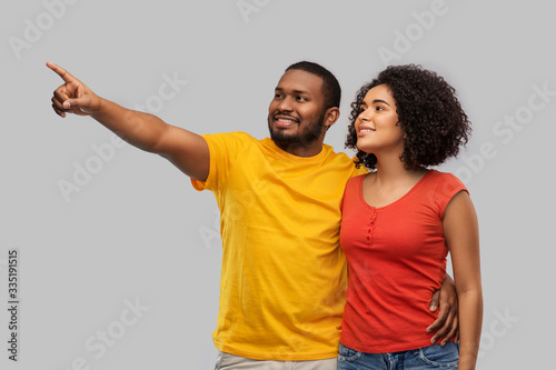 relationships and people concept - happy african american couple pointing finger to something over grey background