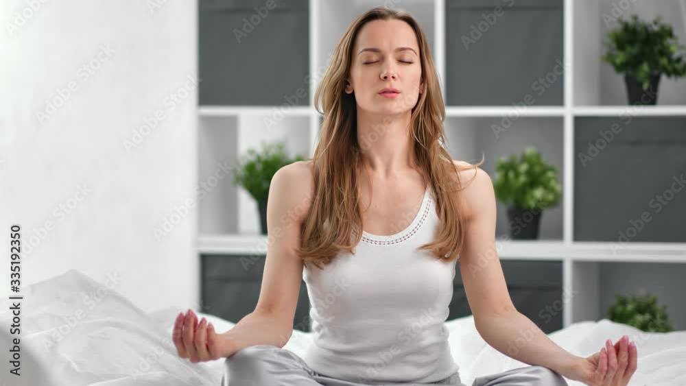 Relaxed woman meditating sitting in lotus position on bed. Shot on RED Raven 4k Cinema Camera Relaxed woman meditating sitting in lotus position on bed. Shot on RED Raven 4k Cinema Camera