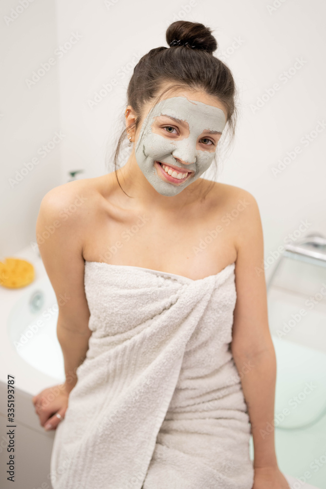 Naklejka premium Woman with clay mask taking selfie with mobile phone at home enjoying relaxation. Beautiful lady doing skincare treatment and taking selfie.Self quarantine & social distancing at home concept.