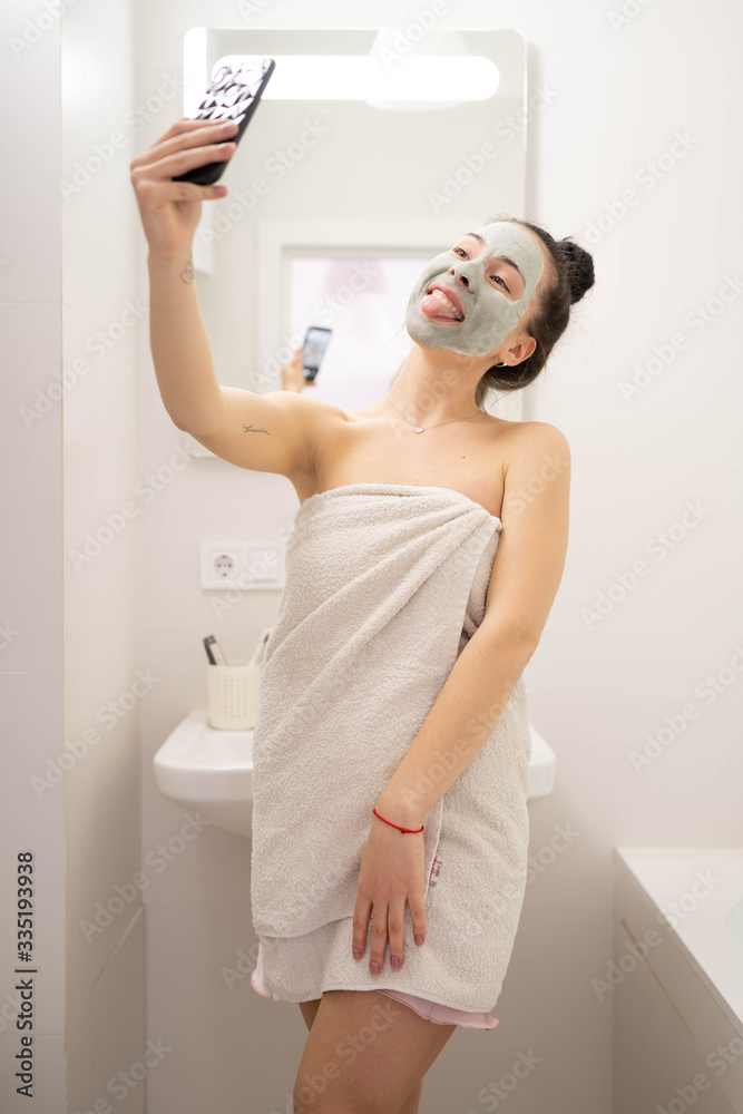 Woman with clay mask taking selfie with mobile phone at home enjoying relaxation. Beautiful lady doing skincare treatment and taking selfie.Self quarantine & social distancing at home concept. Woman with clay mask taking selfie with mobile phone at home enjoying relaxation. Beautiful lady doing skincare treatment and taking selfie.Self quarantine & social distancing at home concept.