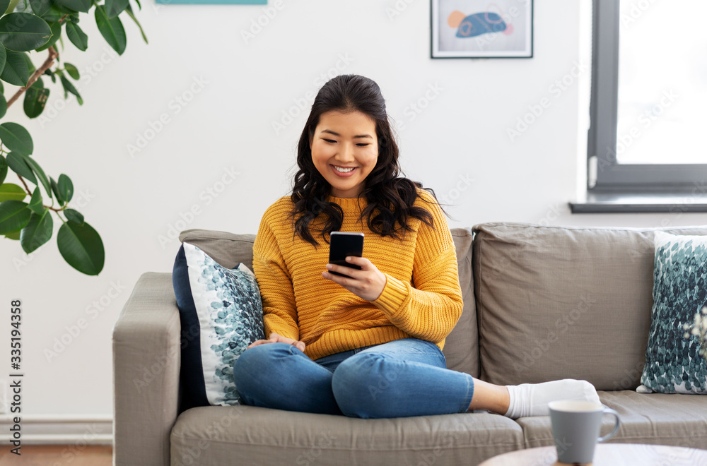 © Syda Productions - people, technology and leisure concept - happy smiling asian young woman in yellow sweater with smartphone sitting on sofa at home © Syda Productions - people, technology and leisure concept - happy smiling asian young woman in yellow sweater with smartphone sitting on sofa at home