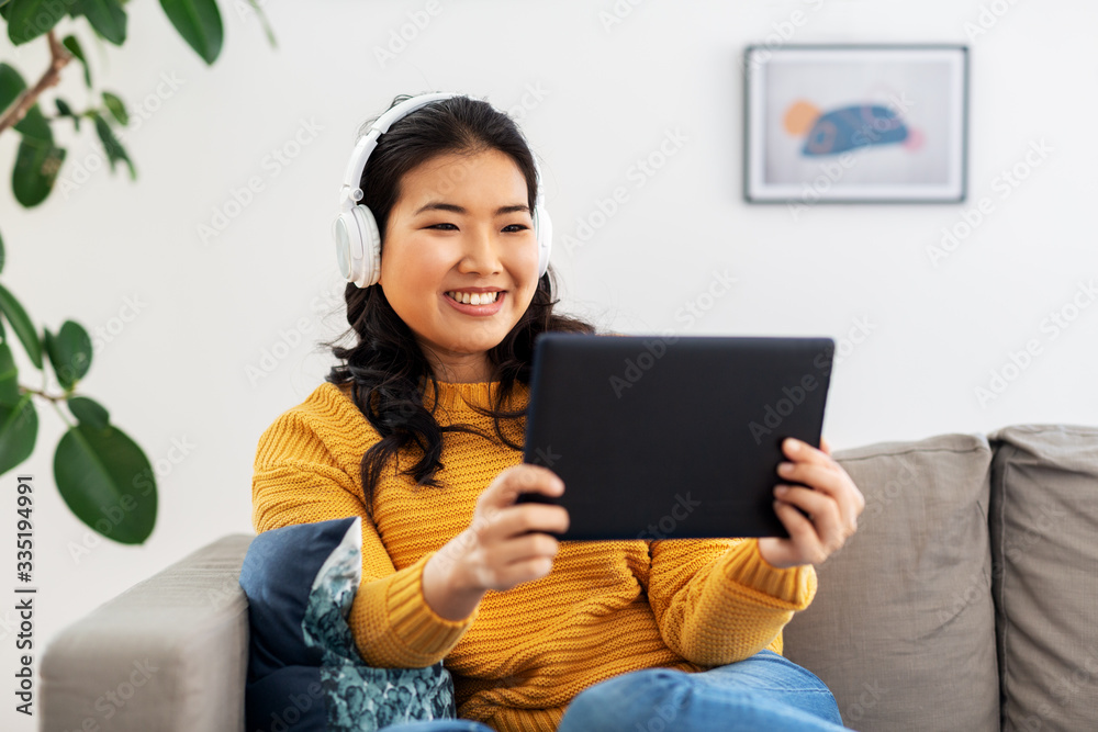 people and leisure concept - happy smiling asian young woman in headphones listening to music on tablet pc computer at home people and leisure concept - happy smiling asian young woman in headphones listening to music on tablet pc computer at home