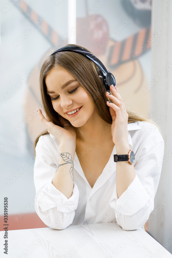 Smiling young woman at the cafe with headphones listening to music