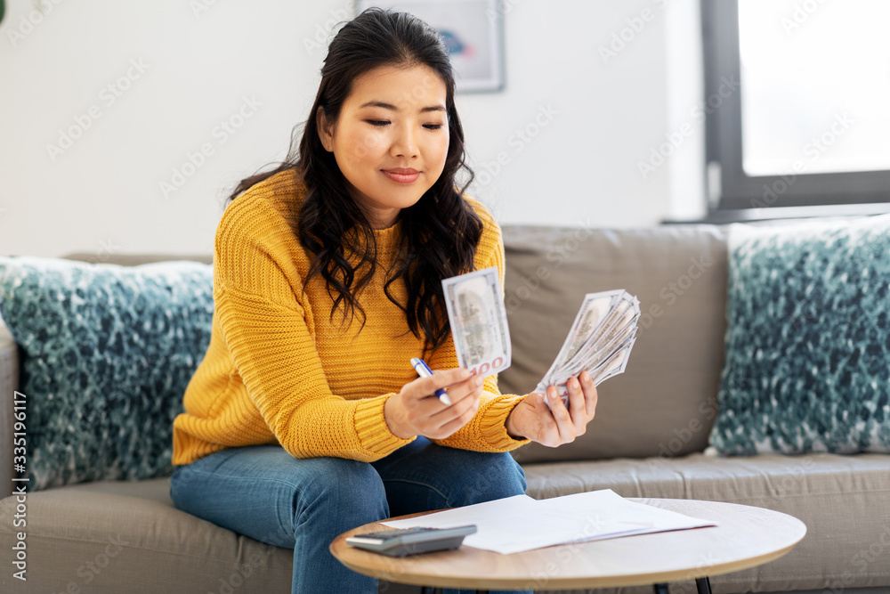 accounting, taxes and finances concept - young asian woman with papers and calculator counting money at home accounting, taxes and finances concept - young asian woman with papers and calculator counting money at home