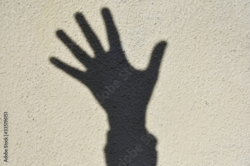 Una sombra de mano sobre pared blanca. Silueta de la palma de una mano con los dedos extendidos. Símbolo de saludo.