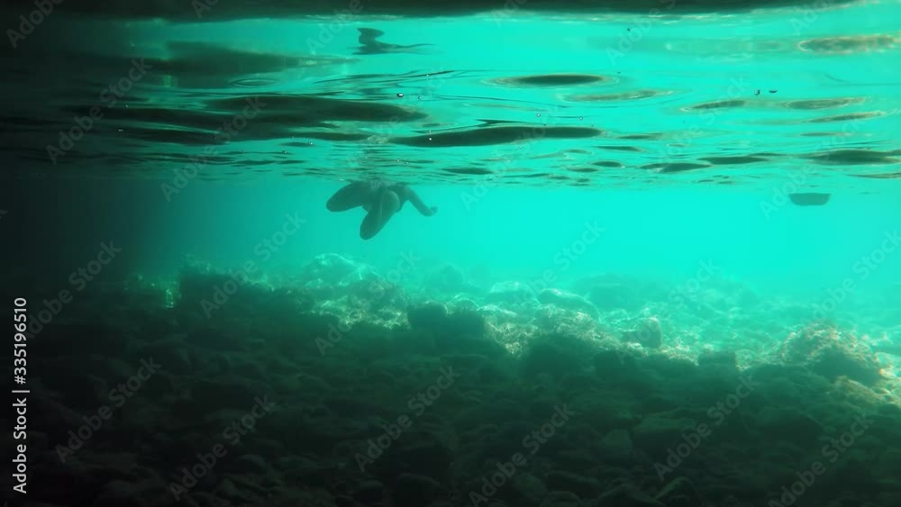 Underwater shot of a female swimmer swimming in sea from darkness toward light Underwater shot of a female swimmer swimming in sea from darkness toward light