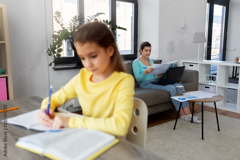 children, education and learning concept - mother with papers and laptop computer working at home office and daughter studying children, education and learning concept - mother with papers and laptop computer working at home office and daughter studying