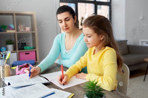 education, family and homework concept - happy mother and daughter with book writing to notebook at home
