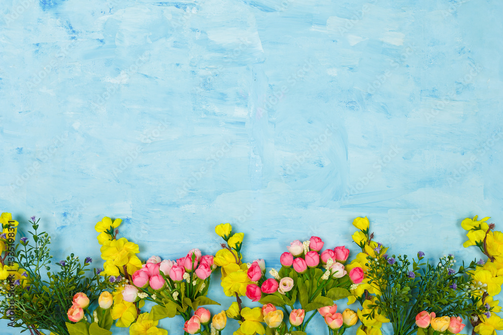 Obraz Artificial pink and yellow flowers on blue painted wooden background. Spring blossom, Easter, women day, mothers day, 8 March concept. Copy space.