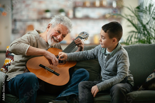Grandpa and grandson playing guitar. Grandfather and grandson enjoying at home.  © JustLife