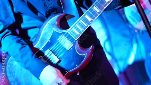Young male guitarist playing guitar at rock concert under stage lights. Musician playing electric guitar on festival with band. Rehearsal on the stage.