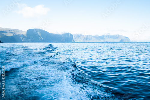 Blue sea with prop wash wake and cliffs in horizon at daytime