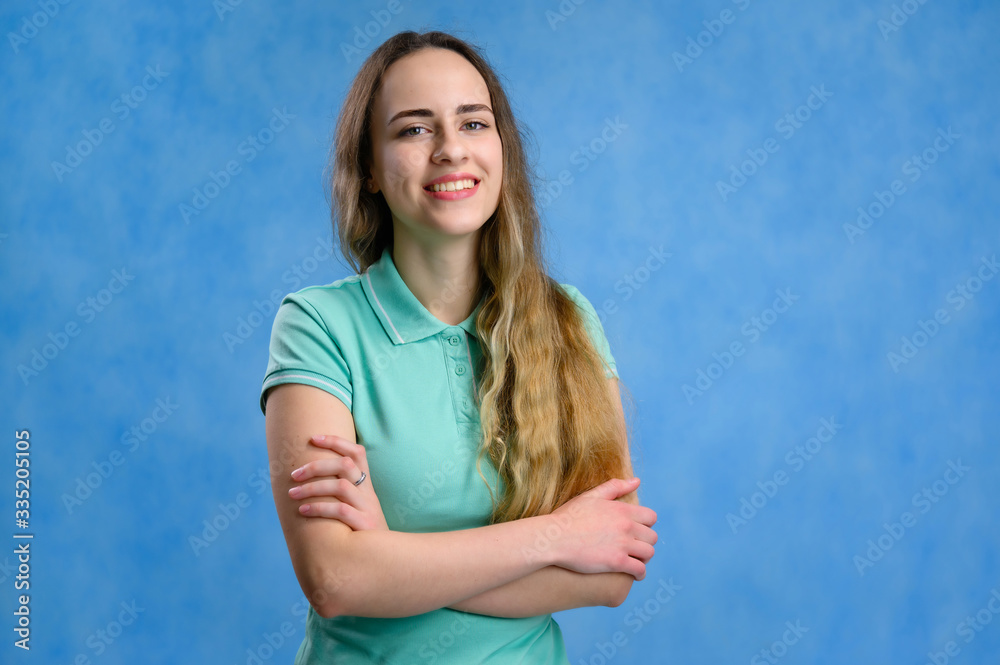 Portrait of a caucasian girl with long hair in a turquoise t-shirt at the camera talking with a smile. Photo taken on a blue background. Portrait of a caucasian girl with long hair in a turquoise t-shirt at the camera talking with a smile. Photo taken on a blue background.