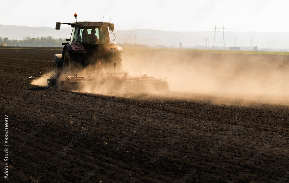 Naklejka premium Tractor is preparing the land at dusk
