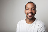 Close-up portrait of young African American young black man wearing T-shirt against white wall with happy face.