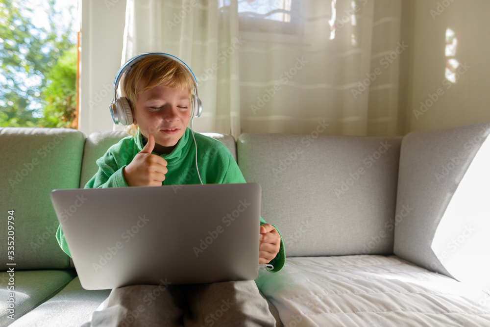 Happy young boy with headphones using laptop and giving thumbs up at home