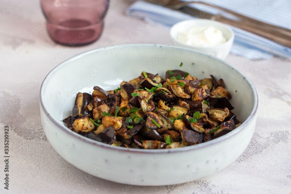 Plate of fried diced eggplants and creme fraiche on grey background. Ready to eat. Plate of fried diced eggplants and creme fraiche on grey background. Ready to eat.