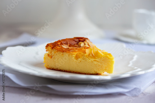 Homemade cheesecake with sliced almonds on plate on grey table. Selective focus, natural light.