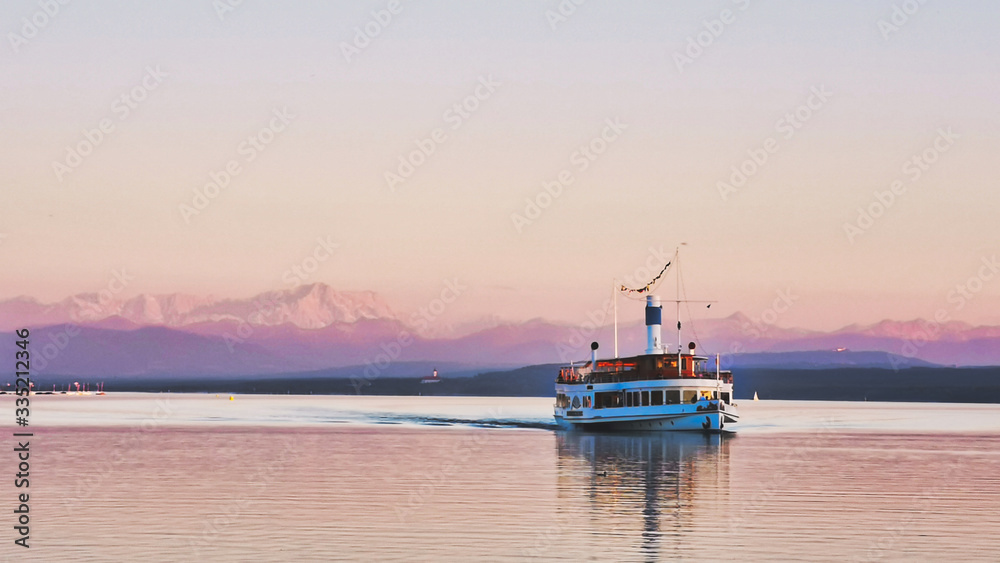 Sunset on a lake with a boat and view of mountains, view of Alps