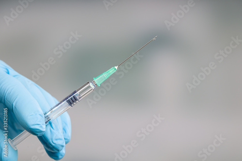 Close up of doctor's hand in medical gloves holding a syringe with a drop of serum at needle photo