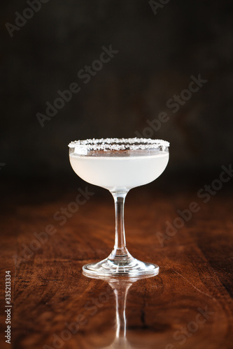 delicious muddy white cocktail in margarita glass with salt at the edges on the dark wooden background, side view, vertical
