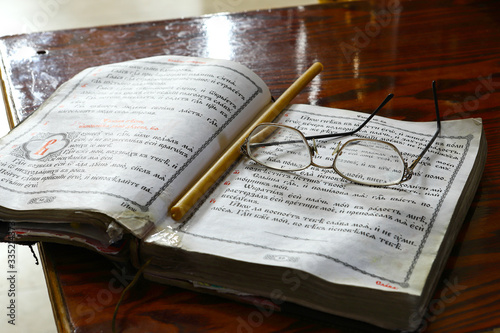 an open old church book in the Old Slavonic language in the Orthodox Church. Orthodox book for a Christian, a cross - a symbol of faith, candles, antique glasses. The concept of the Orthodox faith.