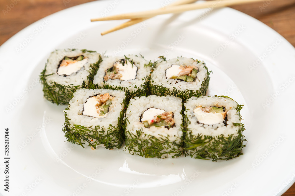 Rolls with salmon and dill on a white plate with chopsticks.