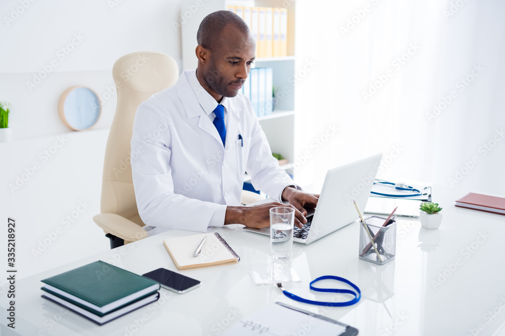 Obraz premium Photo of family doc dark skin guy watch modern technology notebook novelty innovation medical reform cov viral news wear white lab coat sitting chair table office clinic indoors