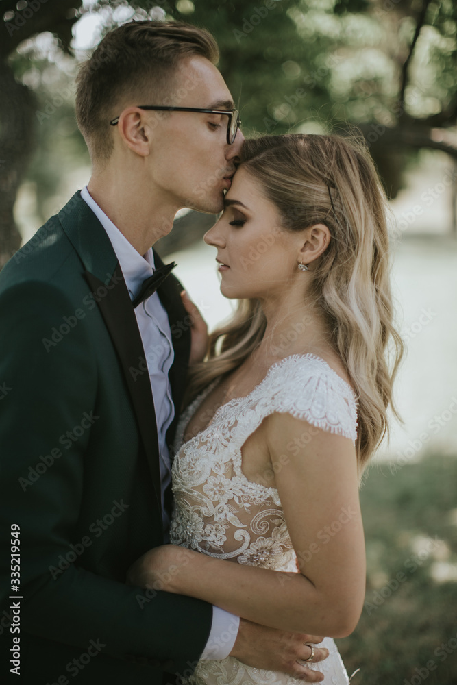 Portrait of a lovely bride and groom embrace, kiss and hug each other. Couple in love in the bosom of nature . Handsome groom and beautiful blonde bride posing in the forest. Modern dress and suit Portrait of a lovely bride and groom embrace, kiss and hug each other. Couple in love in the bosom of nature . Handsome groom and beautiful blonde bride posing in the forest. Modern dress and suit