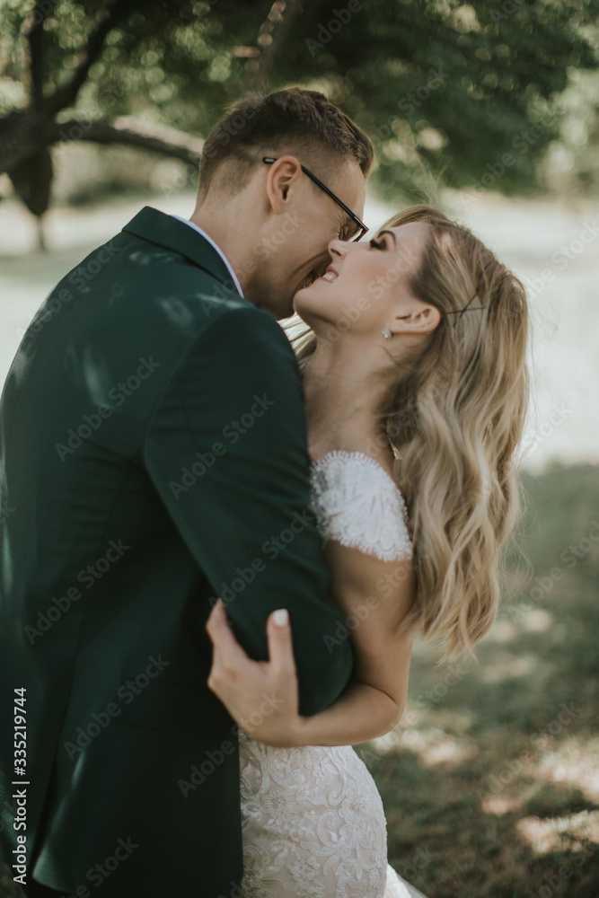 Portrait of a lovely bride and groom embrace, kiss and hug each other. Couple in love in the bosom of nature . Handsome groom and beautiful blonde bride posing in the forest. Modern dress and suit Portrait of a lovely bride and groom embrace, kiss and hug each other. Couple in love in the bosom of nature . Handsome groom and beautiful blonde bride posing in the forest. Modern dress and suit