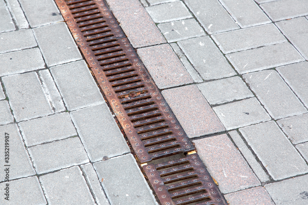 A rust lattice of a drainage paving system on a walkway made of square stone tiles, close up of a rainwater drainage system, nobody.