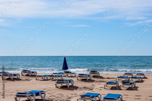 empty deck chairs by the sea, background with sea waves, sand and blue sky © vyudin