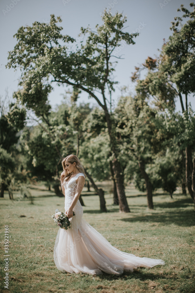 Portrait of a wedding bride walking in a white modern hipster dress. Caucasian blonde bride in a vintage dress in the forest on sunset. Attractive lady posing with a bouquet of flowers Portrait of a wedding bride walking in a white modern hipster dress. Caucasian blonde bride in a vintage dress in the forest on sunset. Attractive lady posing with a bouquet of flowers