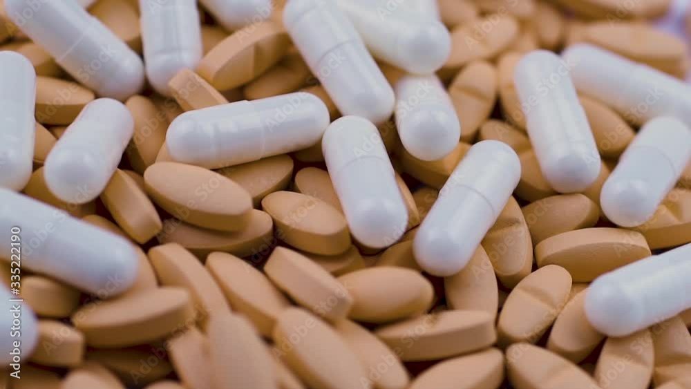 White painkiller capsules are scattered on top of orange oval tablets. White painkiller capsules are scattered on top of orange oval tablets.