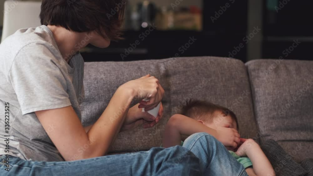 Pretty mother giving some pills to a son laying on a couch. The parent wants to protect the child from coronavirus. Pretty mother giving some pills to a son laying on a couch. The parent wants to protect the child from coronavirus.