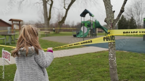 A Little Girl Standing Outside A Yellow Police Tape Barricade Observing At The Closed Playground Due To COVID-19 Spread In Spencerport, New York, USA - Medium shot photo